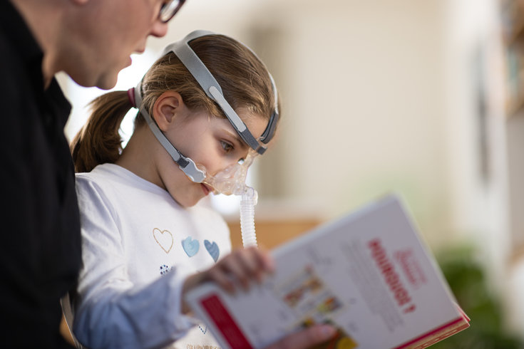 Criança em ventilação mecânica não invasiva lendo um livro infantil
