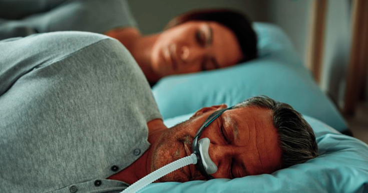 Homem dormindo com sua máscara nasal ao lado da esposa