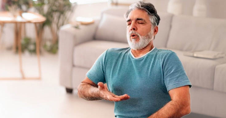 Homem sentado praticando exercícios respiratórios em sua casa