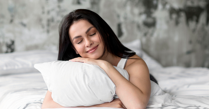 Mulher abraçada ao seu travesseiro e despertando feliz após uma noite boa de sono